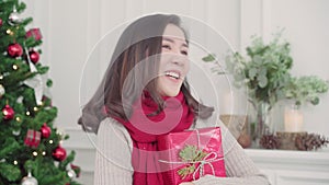 Cheerful happy young Asian woman holding christmas gifts smiling to camera in her living room at home in Christmas Festival.