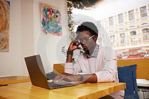 Cheerful and happy young black teenager messaging online on laptop, checking social media news feed, using free wireless
