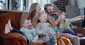 Cheerful happy young Caucasian family with three cute children laugh watching movies at home on the couch slow motion.