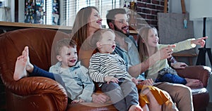 Cheerful happy young Caucasian family with three cute children laugh watching movies at home on the couch slow motion.