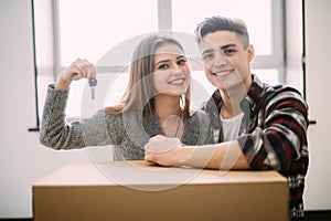 Cheerful and happy young couple holding the keys of their new home with moving cardboard box during move into new apartment