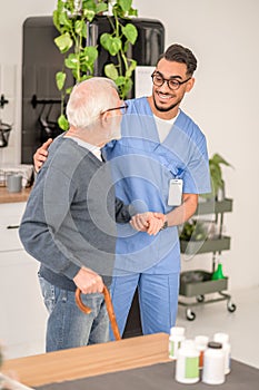 Cheerful healthcare worker supporting an old man with a cane