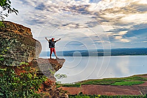 Cheerful hiker gesture raised arms on edge of cliff, on a top of the rock mountain