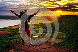 Cheerful hiker gesture raised arms on edge of cliff, on a top of the rock mountain at sunset