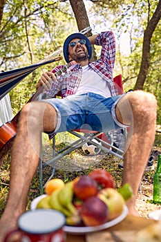Cheerful hipster man enjoying his time in nature. Summertime camping and picnic in forest. Holiday, leisure, fun, lifestyle