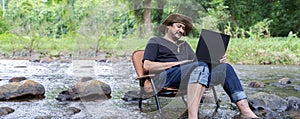 Cheerful hipster man happy with laptop sitting outdoors in nature, freedom and happiness concept, nature against background of