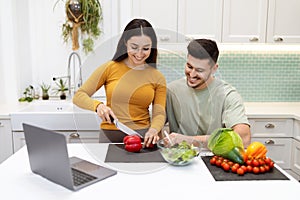 Cheerful hispanic couple looking for recipe on Internet, using laptop