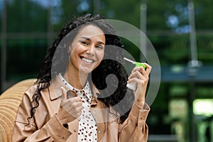 Hispanic woman smiling, using throat spray outdoors photo