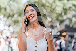 Cheerful Hispanic woman speaking on smartphone in park