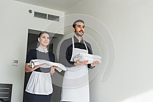 cheerful housekeepers holding white bed sheets