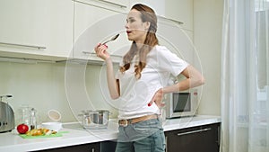 Cheerful housewife cooking soup for dinner. Beautiful happy woman tasting soup