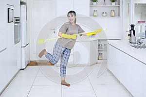 Cheerful housewife playing guitar with a broom