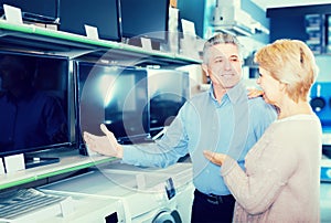 Cheerful husband and wife choose for themselves TV in center of photo