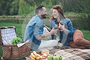 Cheerful husband and wife having picnic near water