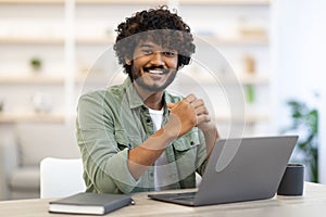 Cheerful indian guy programmer posing at workdesk