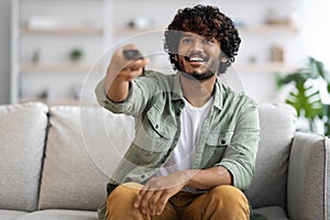 Cheerful indian guy sitting on couch, watching TV