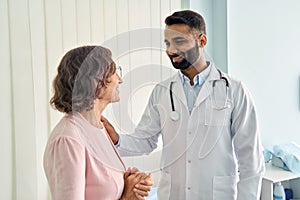 Cheerful Indian latin doctor consulting female older patient in hospital.