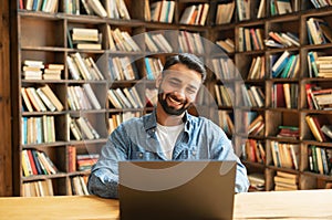 Cheerful Indian male freelancer looks at the laptop screen