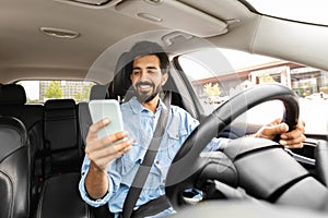 Cheerful indian man entrepreneur using cellphone while driving car