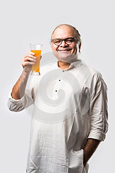 Cheerful Indian old man holding or drinking fresh orange or mango juice in glass