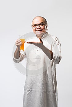 Cheerful Indian old man holding or drinking fresh orange or mango juice in glass