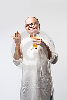 Cheerful Indian old man holding or drinking fresh orange or mango juice in glass