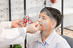 Cheerful Indian-thai boy choosing glasses in optics store, Boy doing eye test checking examination with optometrist using trial