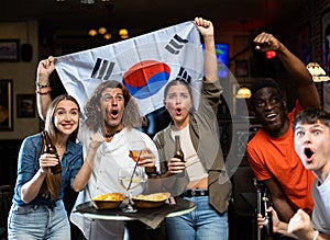 Cheerful international soccer fans waving flag of South Korea with beer and chips in the sport bar