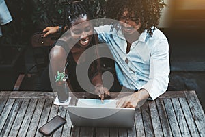 Cheerful interracial couple with laptop in cafe
