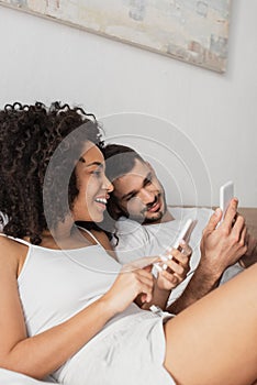 cheerful interracial couple using cellphones in