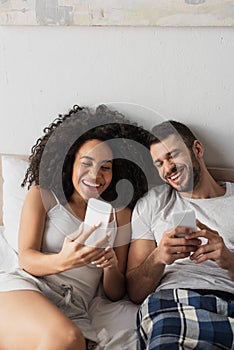 cheerful interracial couple using cellphones and