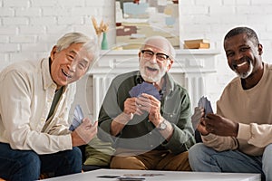 Cheerful interracial friends holding playing cards