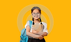 Cheerful Japanese School Girl Hugging Book Standing Over Yellow Background