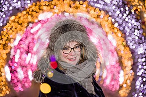 Portrait of cheerful joyful smiling girl in a winter fur cap against the background of night illumination in the winter in Moscow photo