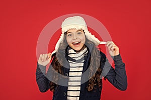 cheerful kid with curly hair in earflap hat. teen girl on red background.