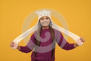 cheerful kid in earflap hat on yellow background, fashion