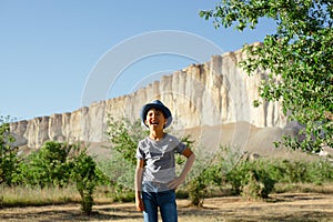 A cheerful kid in jeans, a T-shirt and a blue hat is playing in the garden among the apple trees.