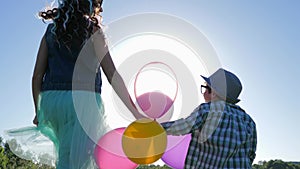 Cheerful kids jumping holding hands with colored balloons against blue sky