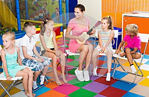 Cheerful kids listening teacher playing small guitar