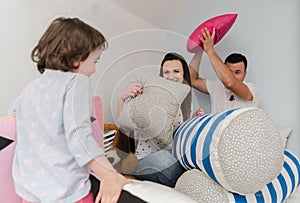 Cheerful kids and parents having pillow fight on bed at home