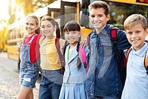 Cheerful kids ready to board school bus, standing outdoors