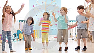 Cheerful kids stand semicircle on floor in kindergarten or day care centre. Preschoolers have fun indoors, playing games