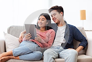 Cheerful Korean Couple Using Digital Tablet Computer Sitting At Home