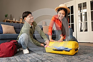 Cheerful Korean Travelers Spouses Packing Travel Suitcase Together At Home