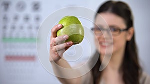 Cheerful lady in glasses showing fresh apple, natural pectin for eyesight, diet