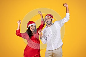 Cheerful latin man and woman in Santa hats, celebrating holiday with raised hands, festive cheer and excitement, dance