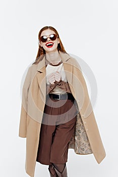 Cheerful laughing cute redhead young woman posing in glasses coat on a white background in the studio. Catalog