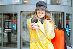 Cheerful laughing woman with shopping bags and credit card against the mall