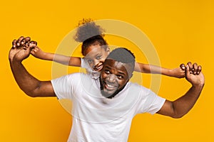 Cheerful little african american girl riding on daddy`s back