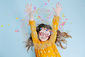 Cheerful little birthday girl lies on a floor, her hands extended up